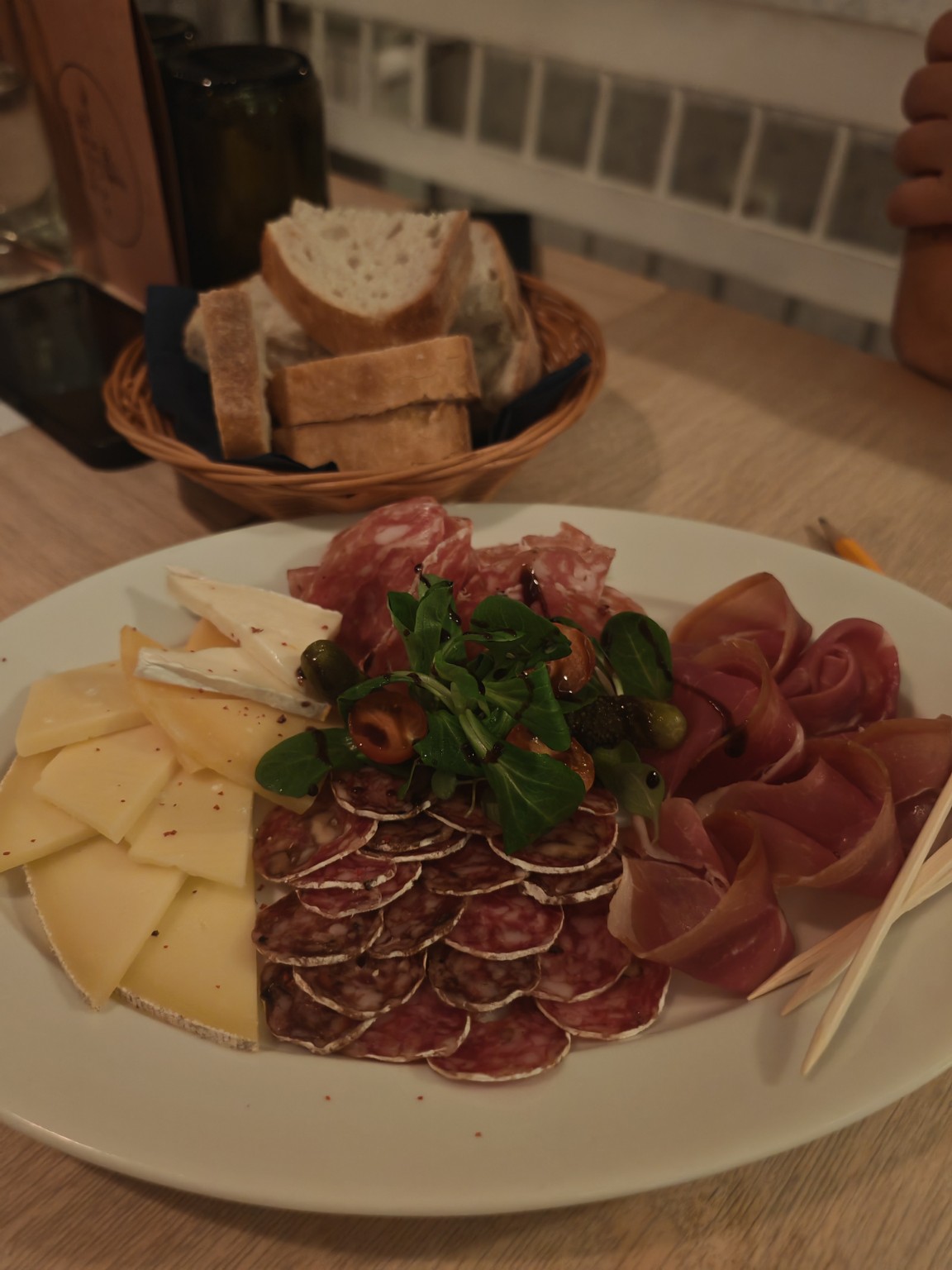 Společný talíř se sýry a uzeninami, vedle košík chleba. Fotografie Jakuba Žákavce.